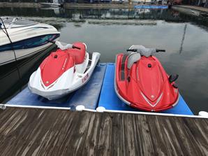 A white-and-red and pure red water scooters parked at a marina dock