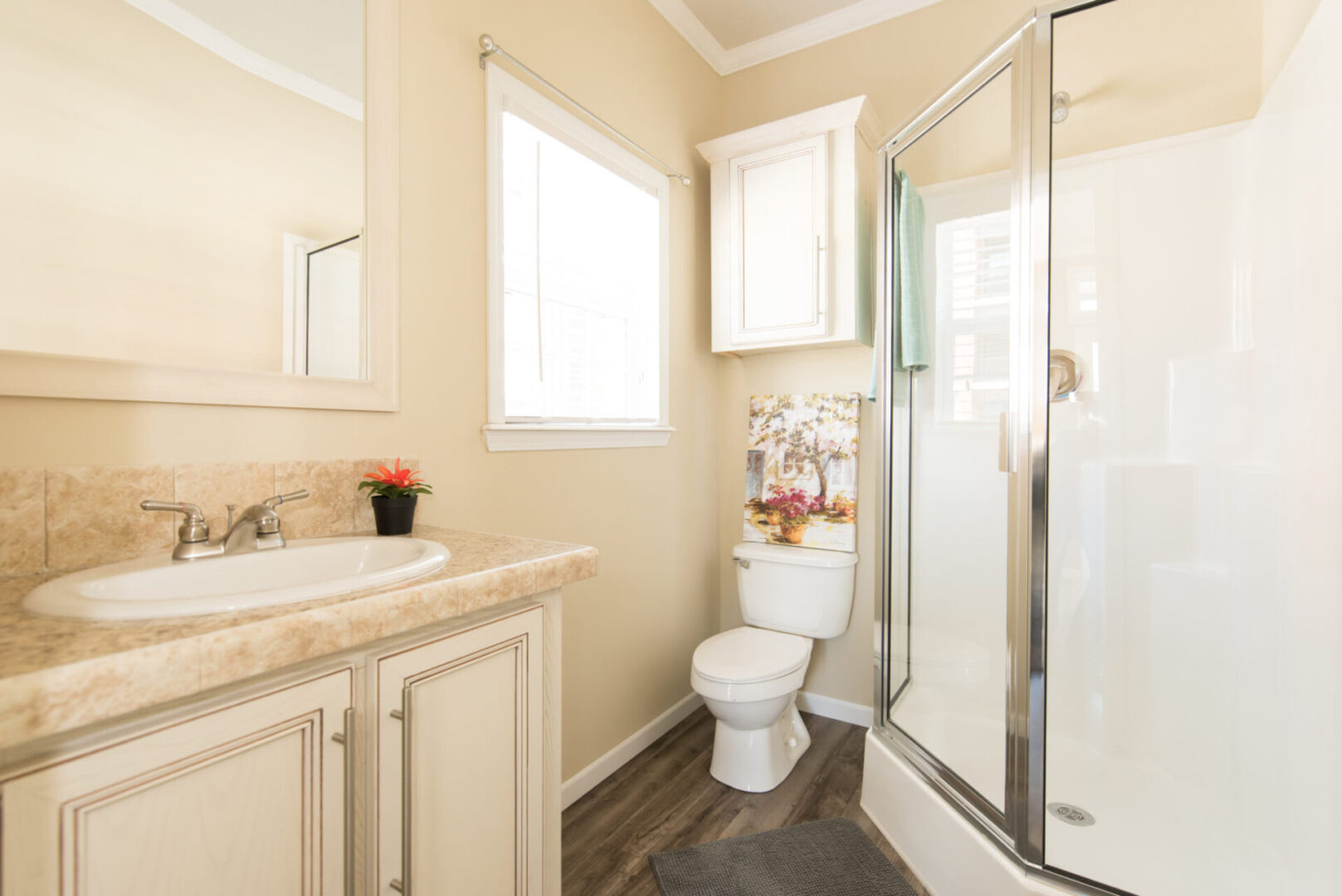 Cream-colored bathroom with a glass shower door, porcelain sink and toilet, and white cabinetries