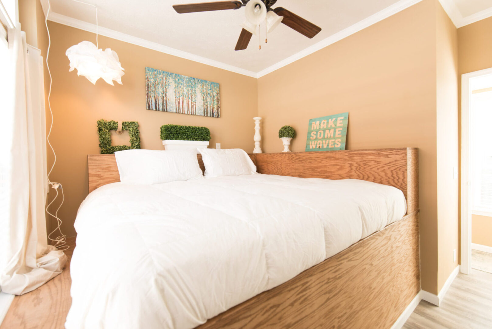Tan-colored bedroom with a high, dark brown, wrap-around bed frame and white bed and a brown ceiling fan