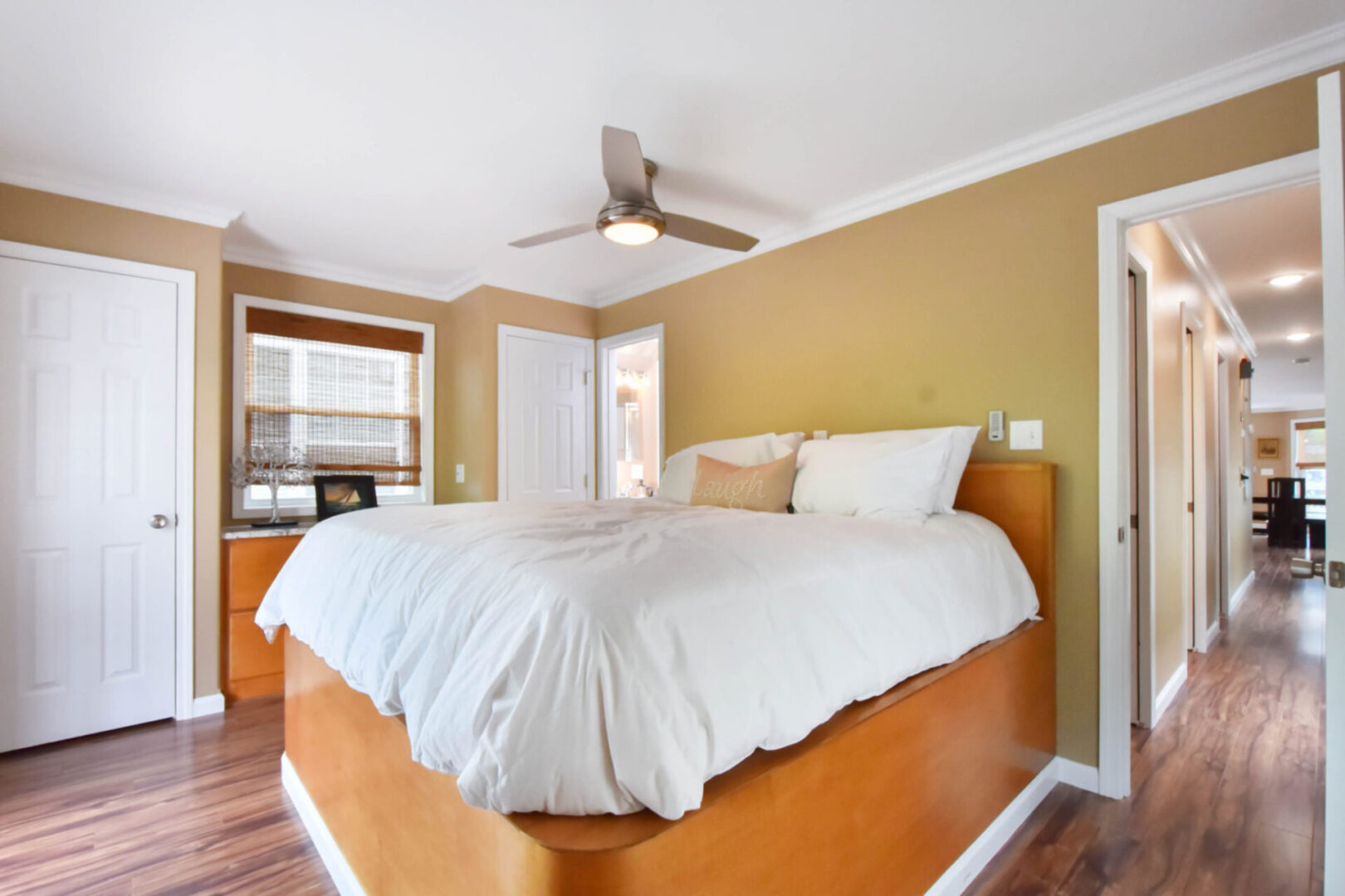 White bed with a tall, brown bed frame in the middle of a tan-colored room