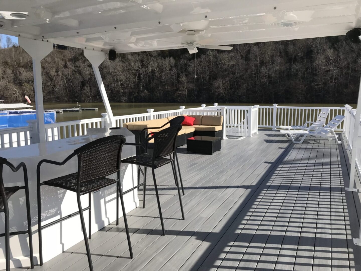 Houseboat roof deck with a pure white bar counter and black woven bar stools, couch set, and white lounge chairs