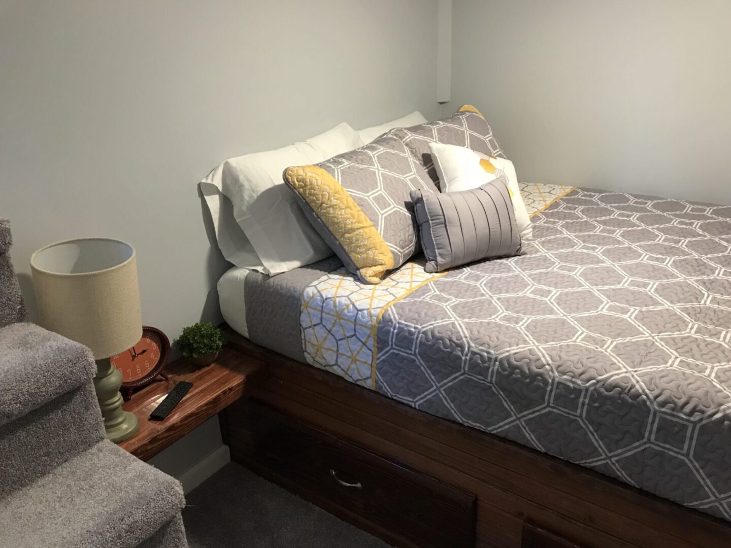 Light grey bedroom walls of a white bed with grey-and-yellow sheet designs on top of a dark brown bed frame