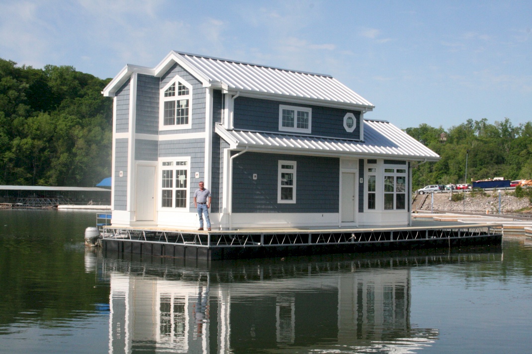 Man standing on a platform of a two-story dark blue houseboat