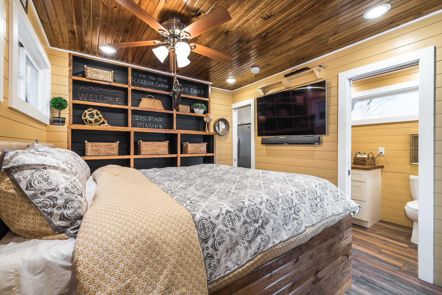 Bed in a wood-paneled bedroom with a wooden modular shelf that has woven artifacts on the shelf tops