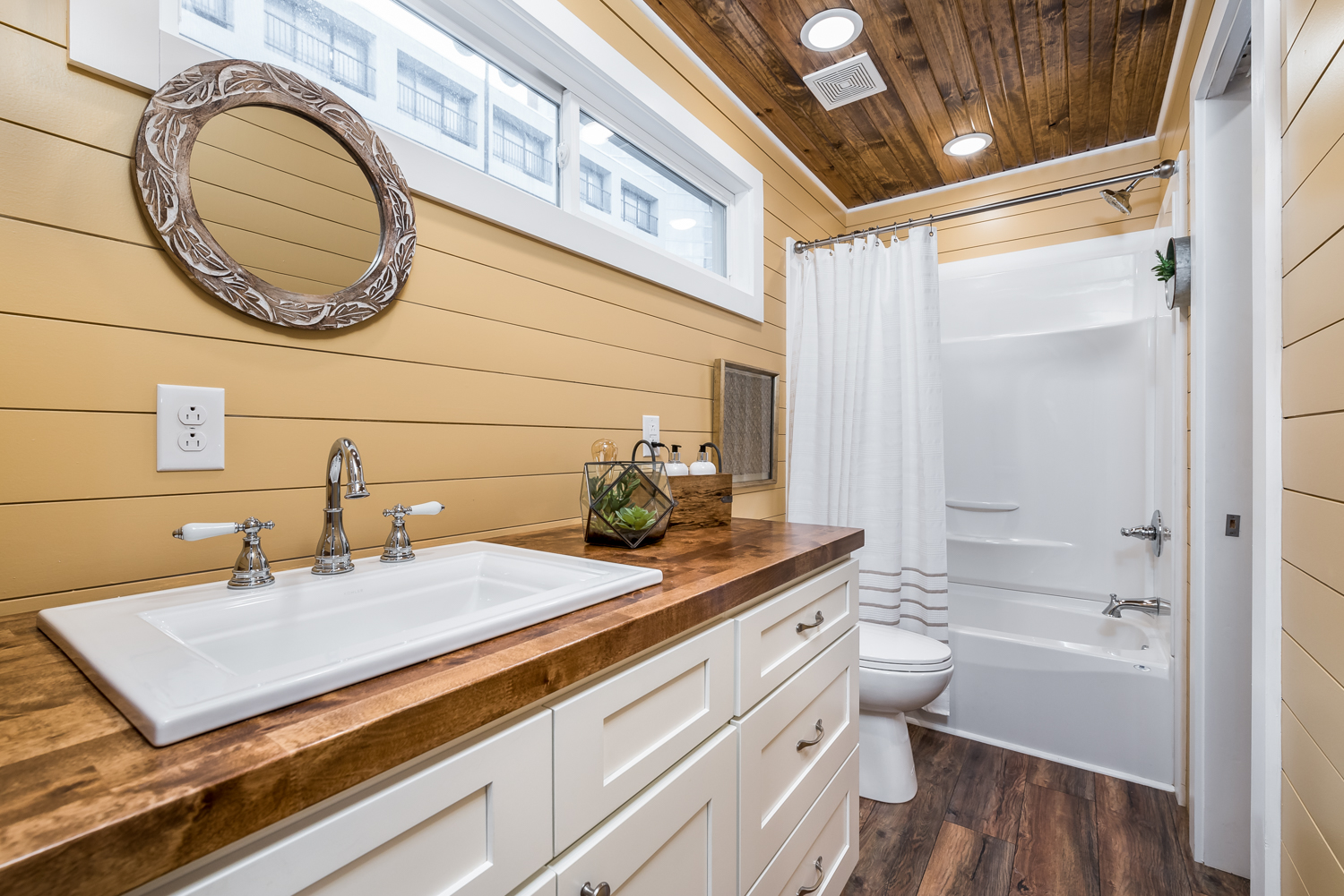 Bathroom with wood panel walls, white bathtub, shower, sink, and cabinetry
