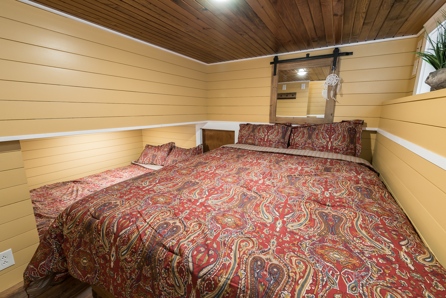 Tan-colored wall paneling in a bedroom with a large bed and a small side bed with matching red bedsheets