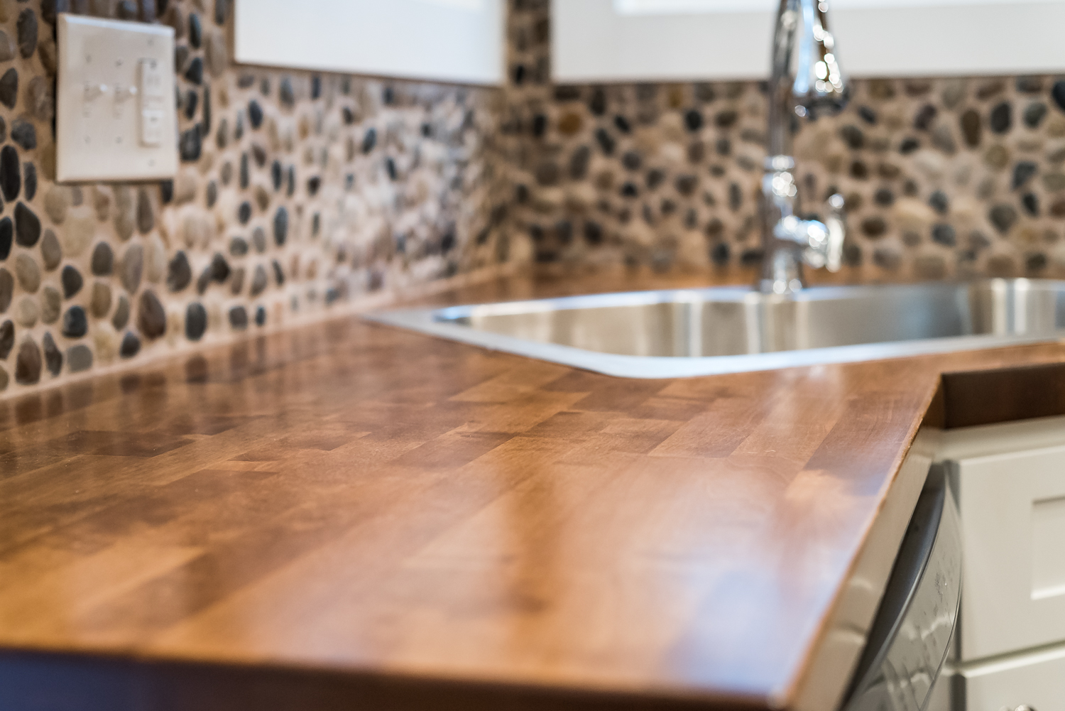 Dark brown wood countertop top with a chrome sink and faucet against a pebble-designed backwall
